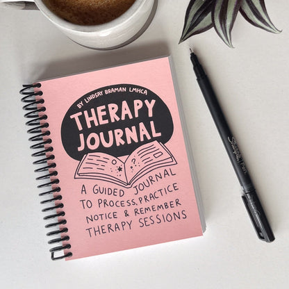 Image of TherapyJournal by Lindsay Braman LMHCA. The journal is palm-sized and spiral bound with a light pink cover.
